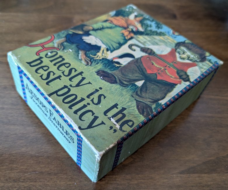 A green box with a bear and a fox on the front, in the foreground is the saying "Honesty is the best policy."
