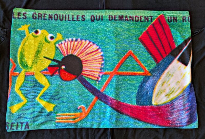 A pillow cover with a frog and a stork on it.