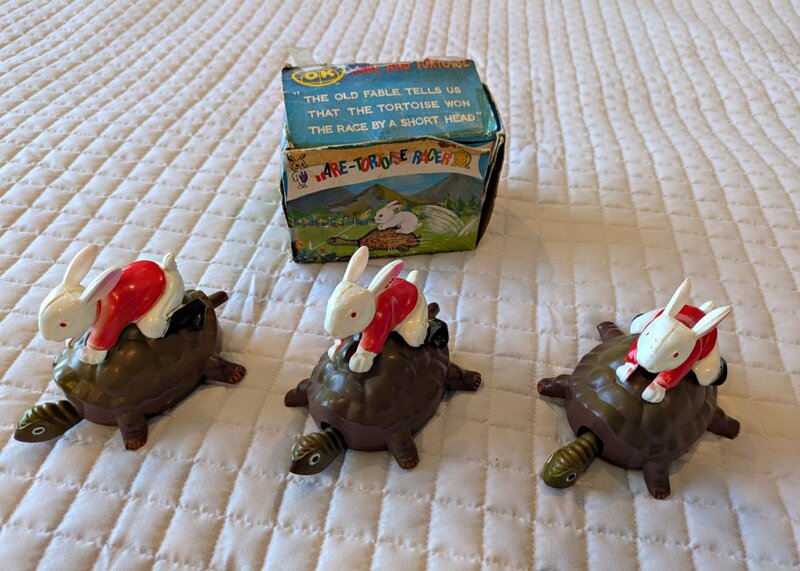 A rabbit wearing a red jacket sitting on a tortoise's back.